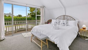 A bedroom with a large bed, a bench, a bedside table, and a view of a balcony with a railing.