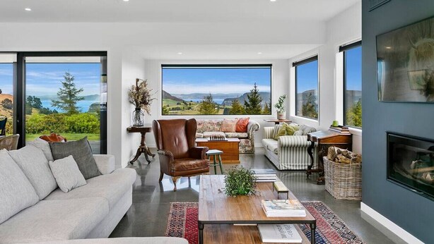 A modern living room with a large window offering a scenic view, a fireplace, and a cozy seating area. - Peaceful Luxury Retreat - with Spa Pool, a spacious, beautiful, private property with stunning views (Taupō)