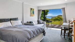A modern bedroom with a large bed, a sofa, a dining table, and a view of the outdoors. - Peaceful Luxury Retreat - with Spa Pool, a spacious, beautiful, private property with stunning views (Taupō)