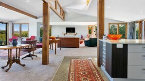 A modern living room with a large TV, a dining area, and a kitchen with a large island. - Ultimate Retreat - Spacious with stunning lake views, natural mineral spa and underfloor heating. (Taupo)
