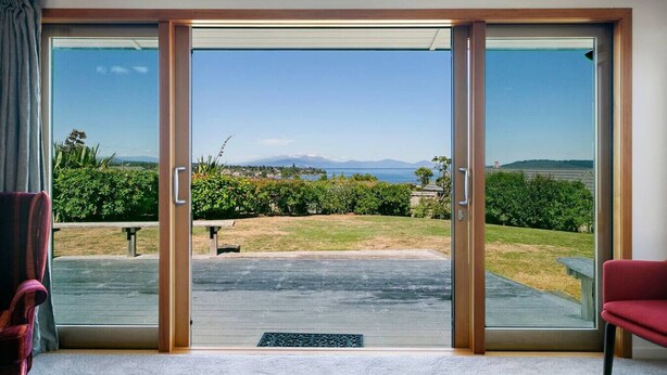 A room with a sliding glass door leading to a backyard with a view of mountains and a body of water. - Ultimate Retreat - Spacious with stunning lake views, natural mineral spa and underfloor heating. (Taupo)