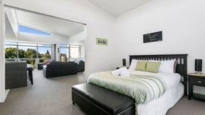 Quarto de hotel moderno com uma cama grande, área de estar com sofá e mesa de jantar, e vista para o exterior.