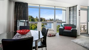 Uma sala de estar moderna com uma mesa de vidro, sofá de couro preto e vista para um lago.