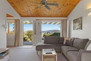 A modern living room with a wooden ceiling, a sofa, a coffee table, and a view through a glass door. - Bellbird Cottage - private large section, with lake and mountain views. Perfect escape to relax (Taupo)