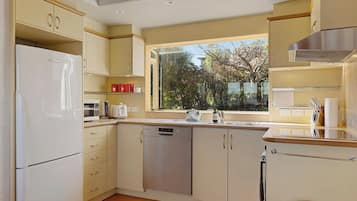 Eine moderne Küche mit Geschirrspüler, Kühlschrank und einem Fenster mit Blick auf Bäume.