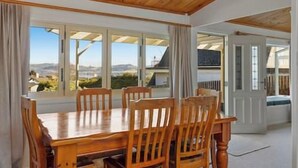 A dining area with a wooden table and chairs, large windows with a view, and a door leading to another room.