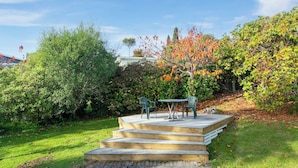 A wooden deck with a table and chairs, surrounded by lush greenery and trees.