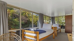 A room with two wooden beds, a wicker chair, and large windows with curtains.