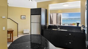 Una cocina moderna con encimera de mármol negro, refrigerador de acero inoxidable y vista al mar a través de un amplio ventanal.