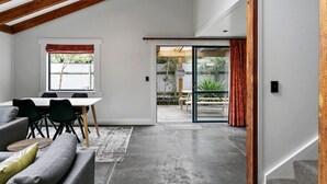 A modern interior with a dining area, a sofa, and a large sliding glass door leading to an outdoor space. - Central and Cozy - popular, peaceful retreat. Two storey, open plan, comfortable living. (Taupō)