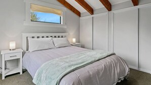 A bedroom with a bed, bedside tables, a window with a view, and a wardrobe. - Central and Cozy - popular, peaceful retreat. Two storey, open plan, comfortable living. (Taupō)