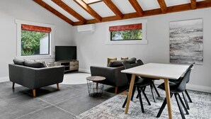 A modern living room with a TV, sofa, and dining table. - Central and Cozy - popular, peaceful retreat. Two storey, open plan, comfortable living. (Taupō)