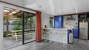A modern kitchen with a bar area, a dining table outside, and a sliding glass door leading to a patio. - Central and Cozy - popular, peaceful retreat. Two storey, open plan, comfortable living. (Taupō)