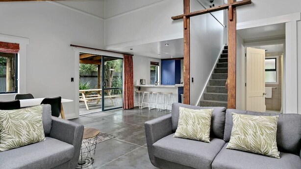 A spacious living area with a large sliding glass door leading to a patio, a kitchen area, and a staircase. - Central and Cozy - popular, peaceful retreat. Two storey, open plan, comfortable living. (Taupō)