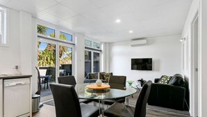 Una sala de estar moderna con una mesa de comedor de vidrio, sillas de cuero negro, un sofá negro y un televisor en la pared.