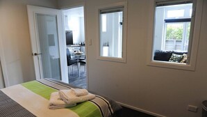 Un dormitorio con cama, dos ventanas y vistas a un comedor.