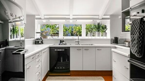 Een moderne keuken met witte kasten, een inbouwvaatwasser en een raam met uitzicht op een tuin.