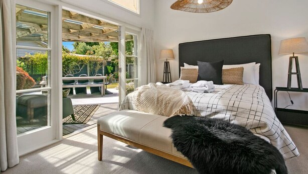 Slaapkamer met een groot bed, twee bedlampen, een bankje en uitzicht op de omgeving via grote glazen deuren.