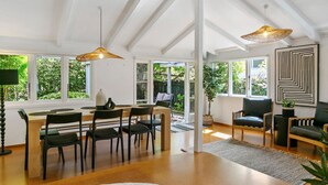 Een moderne eetruimte met een houten tafel en stoelen, grote ramen en uitzicht op groen.