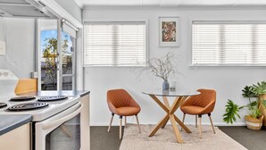A modern kitchen with a stove, a dining table with two chairs, and a window with blinds.