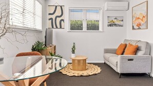 A modern living room with a glass dining table, grey sofa, and a TV on a wooden stand.
