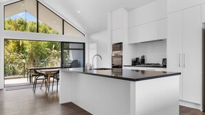 A modern kitchen with a large island, white cabinetry, and a view of greenery outside. - Blue Dun Retreat | Relaxing, Modern Getaway Near Lake & Town (Taupō)