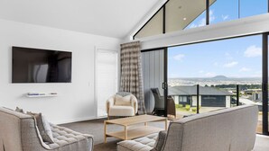 A modern living room with a large TV, comfortable seating, and a view of the city. - Blue Dun Retreat | Relaxing, Modern Getaway Near Lake & Town (Taupō)