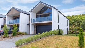 A modern two-story house with a garage, surrounded by a well-maintained lawn and a black metal fence. - Blue Dun Retreat | Relaxing, Modern Getaway Near Lake & Town (Taupō)