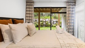 A bedroom with a large bed, a view of a garden through glass doors, and curtains on the windows. - Blue Dun Retreat | Relaxing, Modern Getaway Near Lake & Town (Taupō)