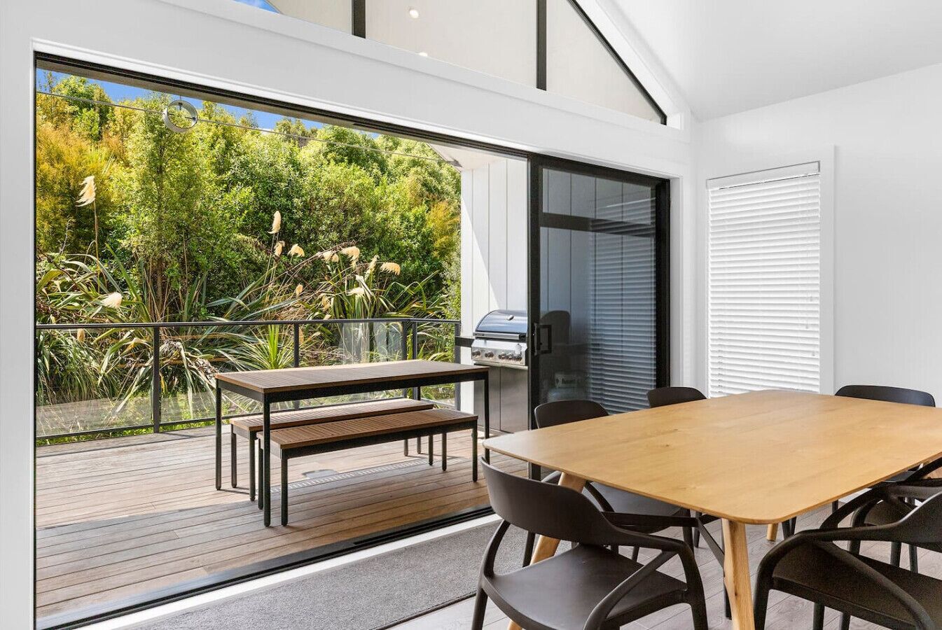 Een moderne eethoek buiten, met een houten tafel, stoelen, een bankje en een barbecue.