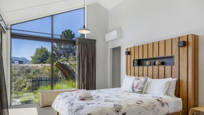 Ein Schlafzimmer mit großem Fenster, einem hölzernen Kopfteil und einem Bett mit floralem Bettbezug.