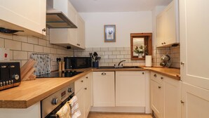 A modern kitchen with white cabinets, a wooden countertop, a built-in oven, a microwave, and a sink. - Triumph Cottage (Chipping Norton)