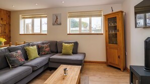 A modern living room with a grey sectional sofa, wooden coffee table, and a cabinet with glass doors. - Triumph Cottage (Chipping Norton)