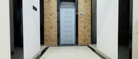 A hallway with a marble floor leading to an elevator with a glass door.