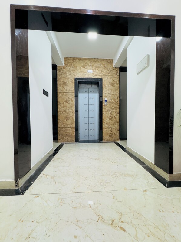 A hallway with a marble floor leading to an elevator with a glass door.