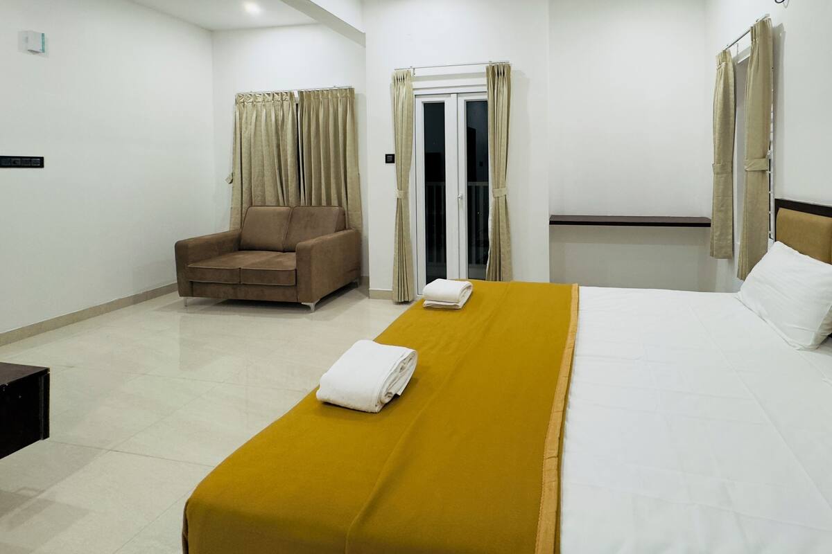 Quarto de hotel com cama, sofá, janela com cortinas e porta.