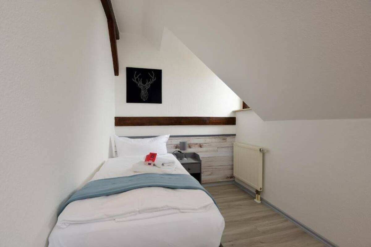 Un dormitorio con cama, mesita de noche, radiador y un cuadro de cabeza de venado colgado en la pared.