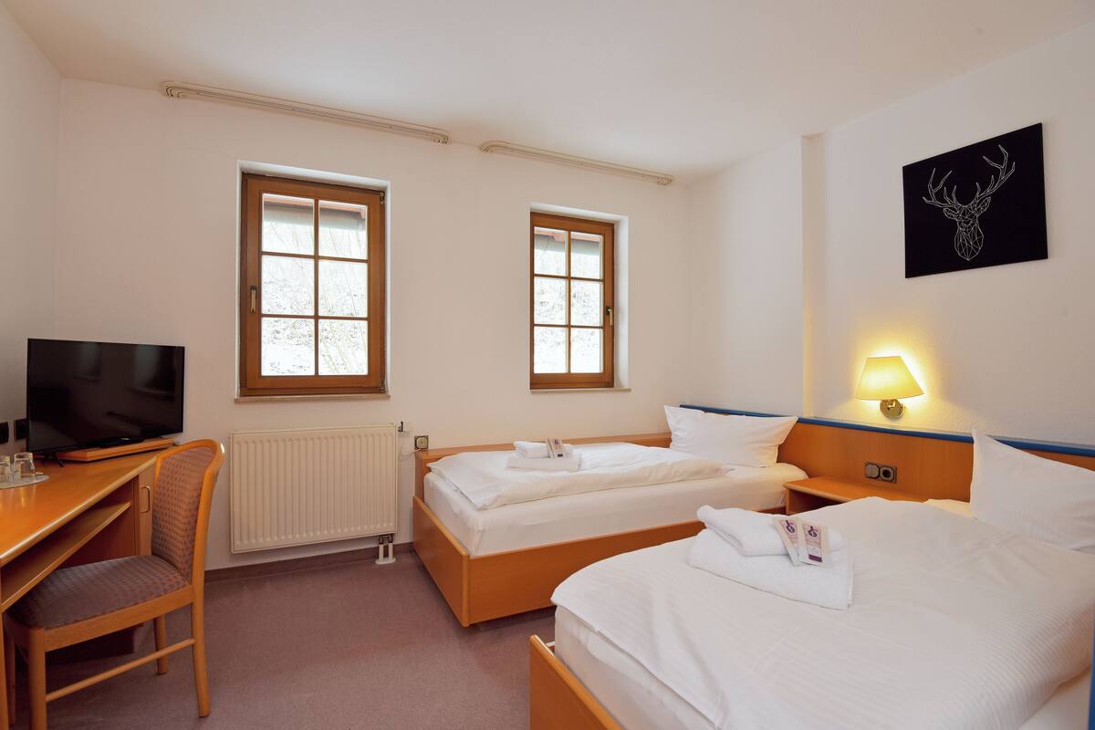 Una habitación de hotel con dos camas, un escritorio con televisor y una ventana.