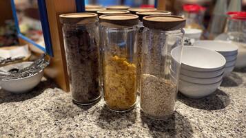 A kitchen counter with jars containing various grains and seeds, a bowl of utensils, and stacked bowls.