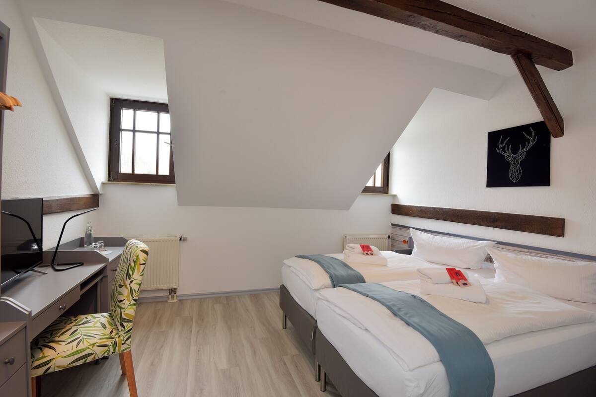 Un dormitorio con escritorio, dos camas, un radiador y una ventana.