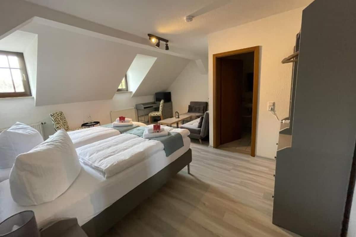 Un dormitorio con una cama grande, un escritorio y una silla. Se ve una ventana y una puerta.