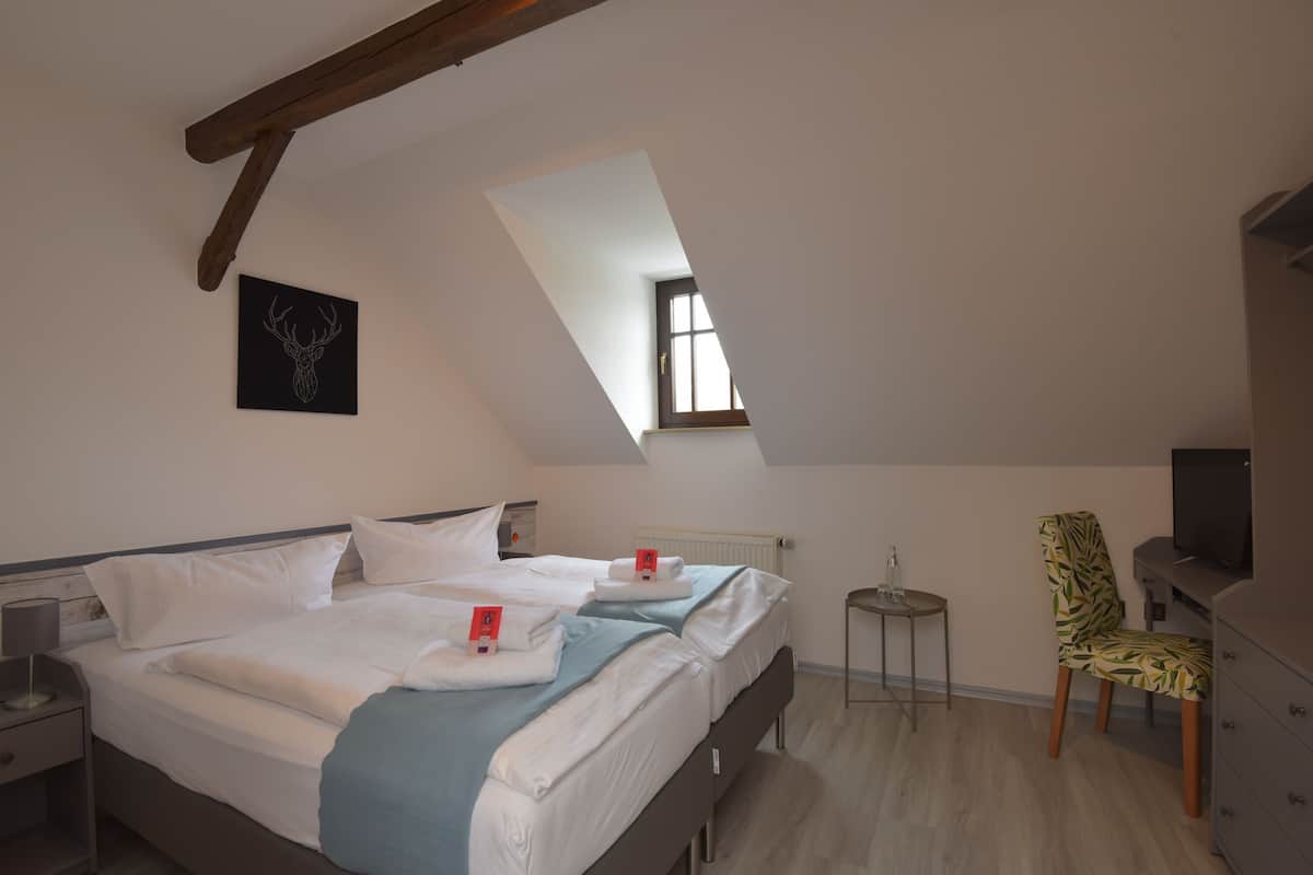 Un dormitorio con dos camas, una mesita, una silla, un televisor y una ventana.