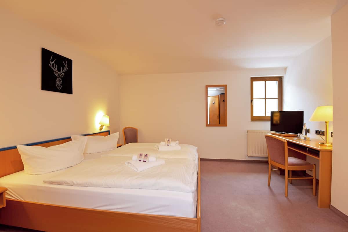 Habitación de hotel con cama, escritorio, silla, televisor y un cuadro colgado en la pared.