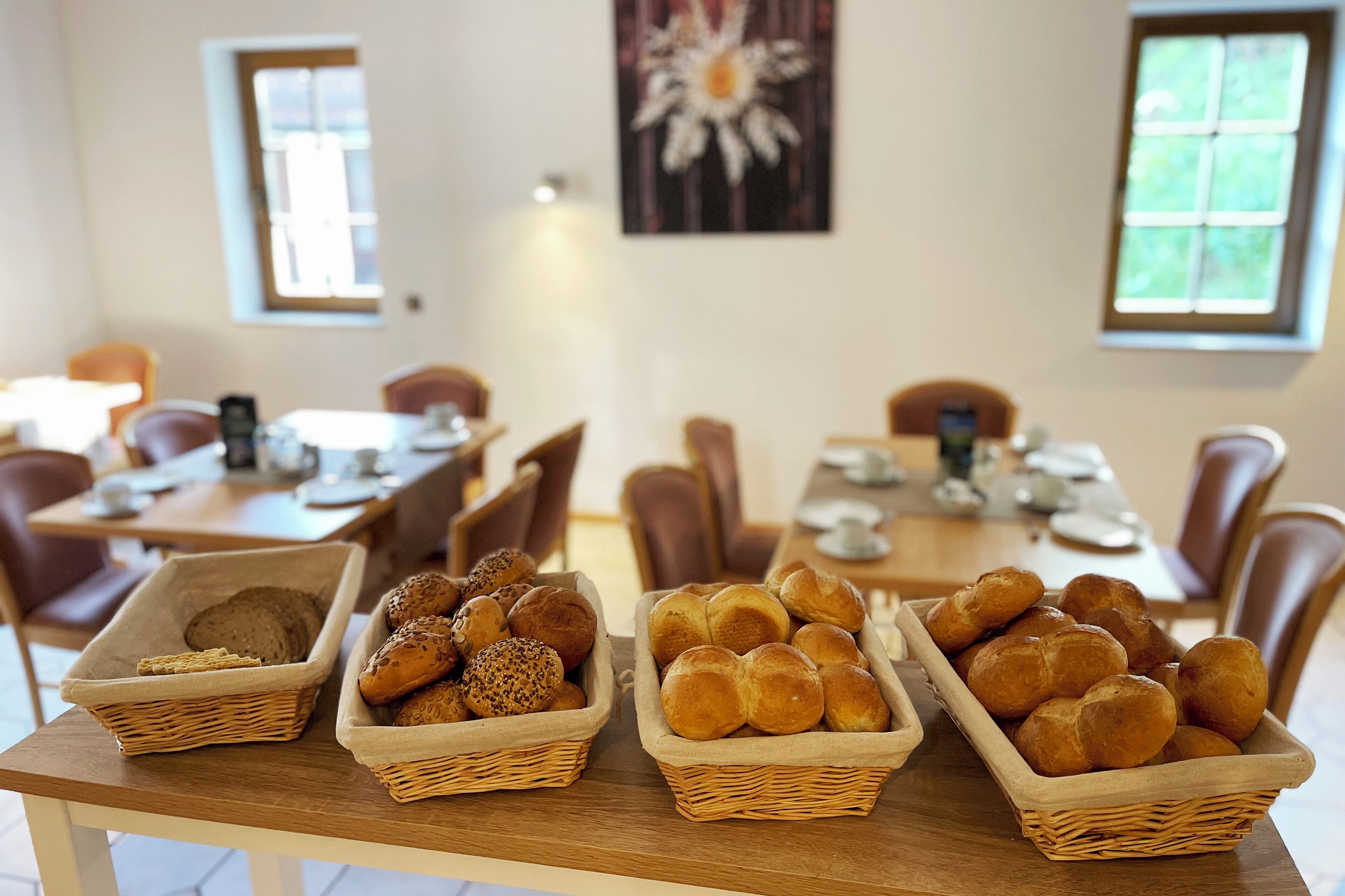 Ein Essbereich mit Körben aus Weidengeflecht, gefüllt mit verschiedenen Brotsorten und Brötchen, auf einem Holztisch.