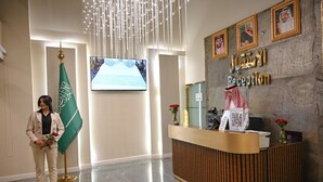 A reception area with a marble floor, a reception desk, a flag, and a screen displaying a video. - Violet Hotel (Yanbu)