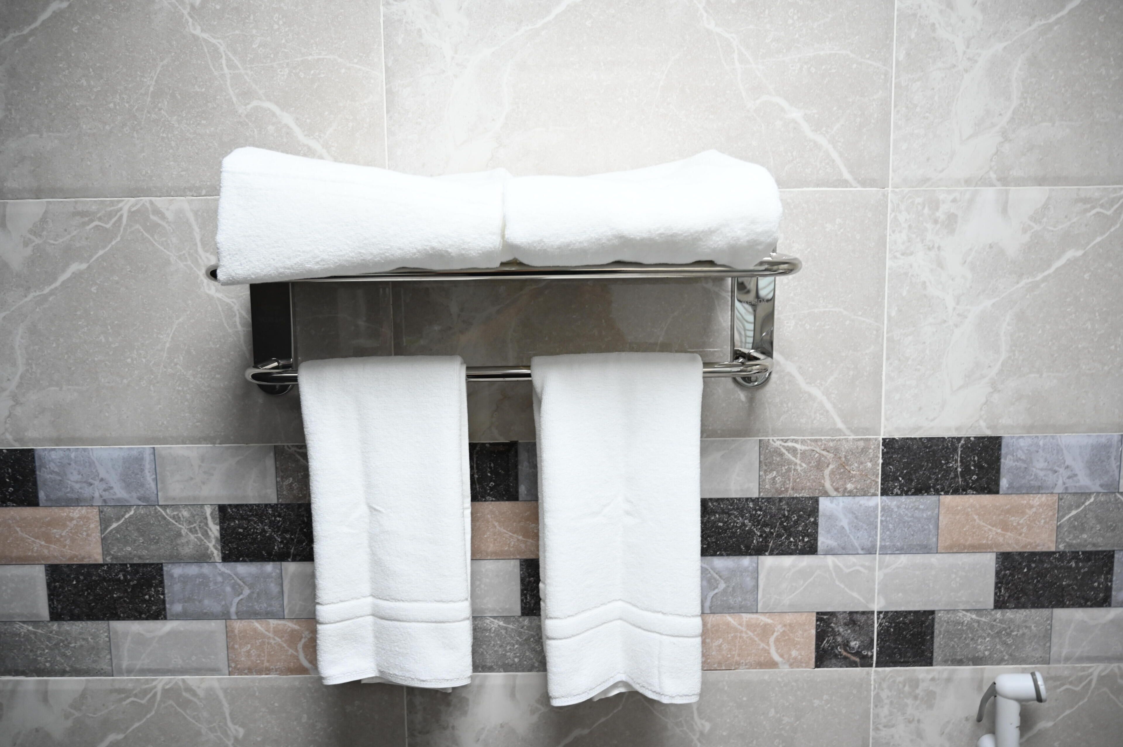 Une salle de bain avec un porte-serviettes sur lequel sont posées deux serviettes, un mur carrelé avec un mélange de carreaux gris et bruns, et une pomme de douche.
