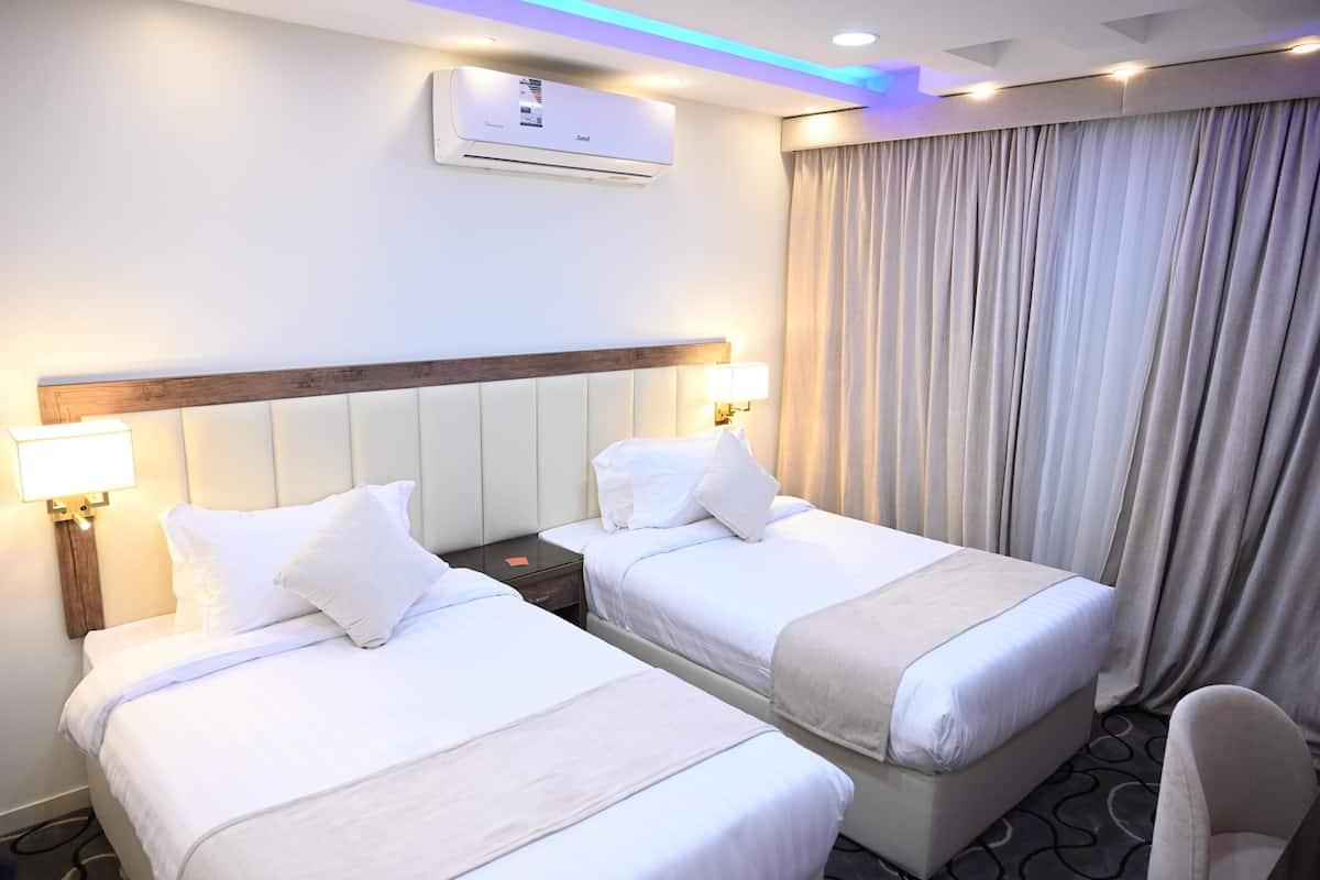 Quarto de hotel com duas camas, mesa de cabeceira, ar condicionado e janela com cortinas.