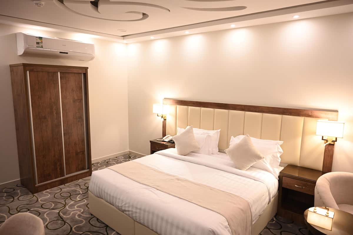 Quarto de hotel com cama, abajures, mesa de cabeceira, guarda-roupa e ar condicionado.