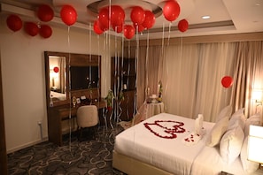 A hotel room with a bed, a desk, a chair, a mirror, and red balloons. - Violet Hotel (Yanbu)