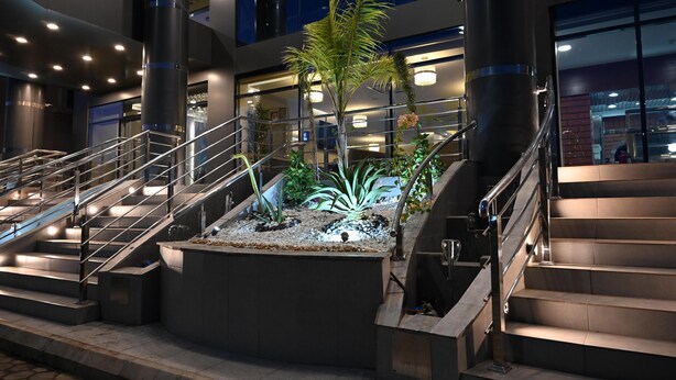 A modern building with a central atrium featuring a staircase, a water feature with plants, and a view of the interior. - Violet Hotel (Yanbu)